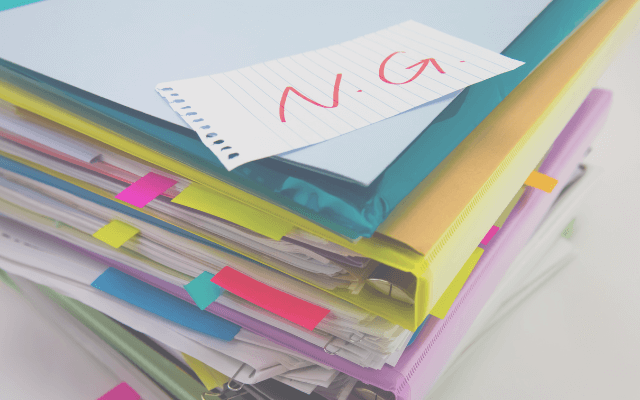 「NG」と書かれたメモがノートやファイルの上に置かれている